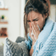 Woman sitting on a sofa, wrapped in a blue blanket, looking distressed and covering her face with her hands, symbolizing the need for mobile healthcare services.
