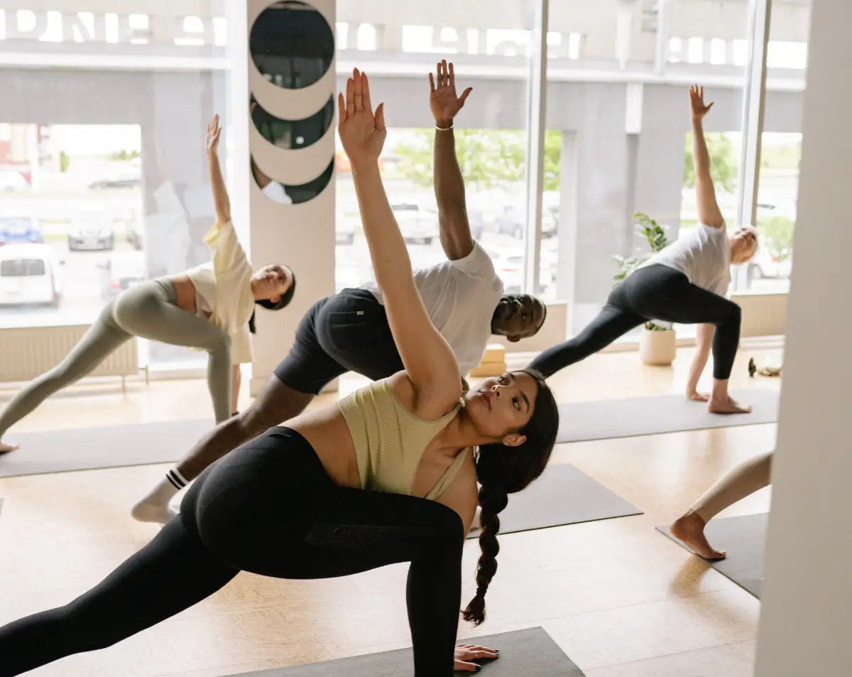 Group of diverse individuals practicing yoga in a bright studio, emphasizing wellness and healthy habits during National Wellness Month.